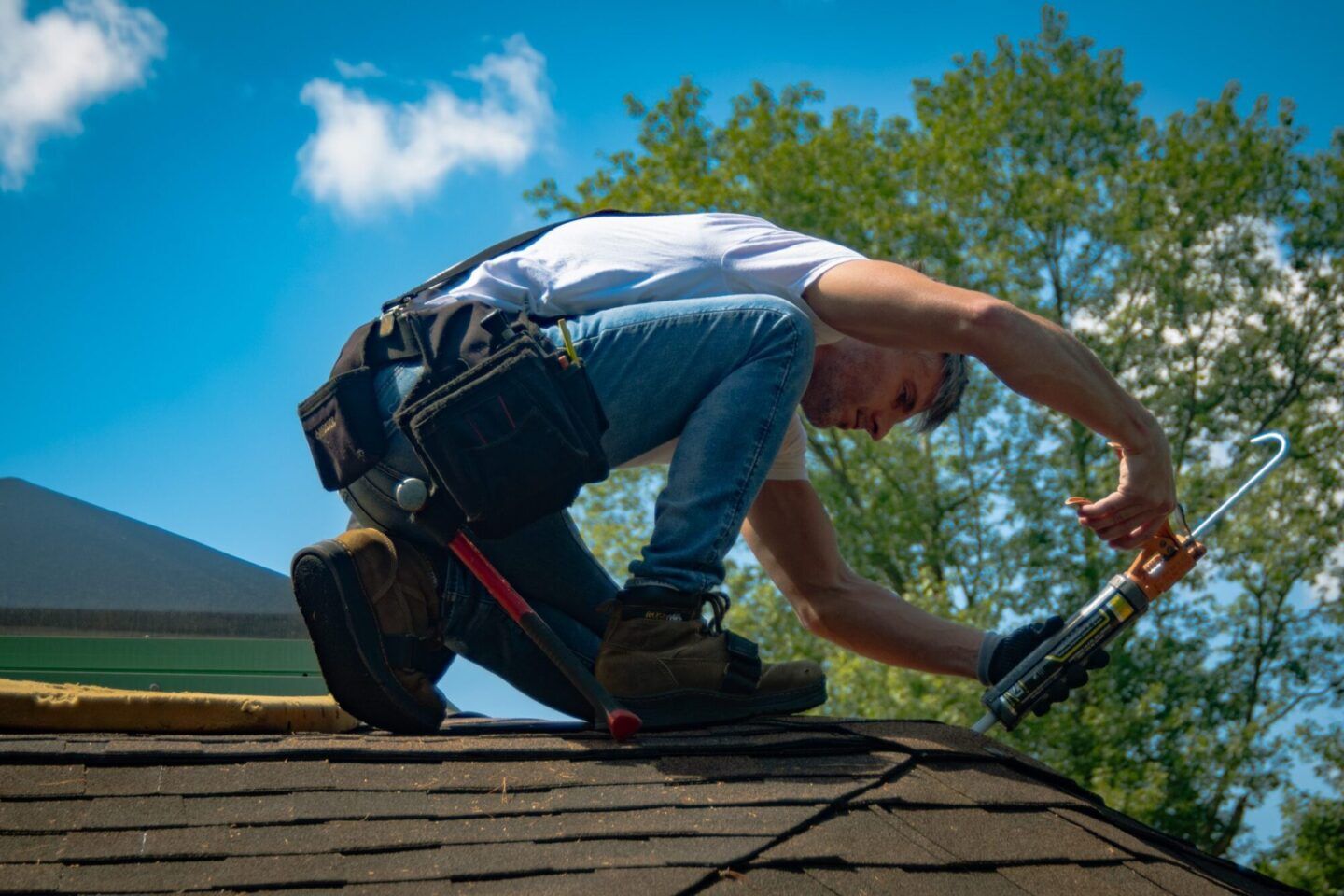 Roof Maintenance: Roofer using caulk gun on shingle roof. Professional home maintenance and repair services.