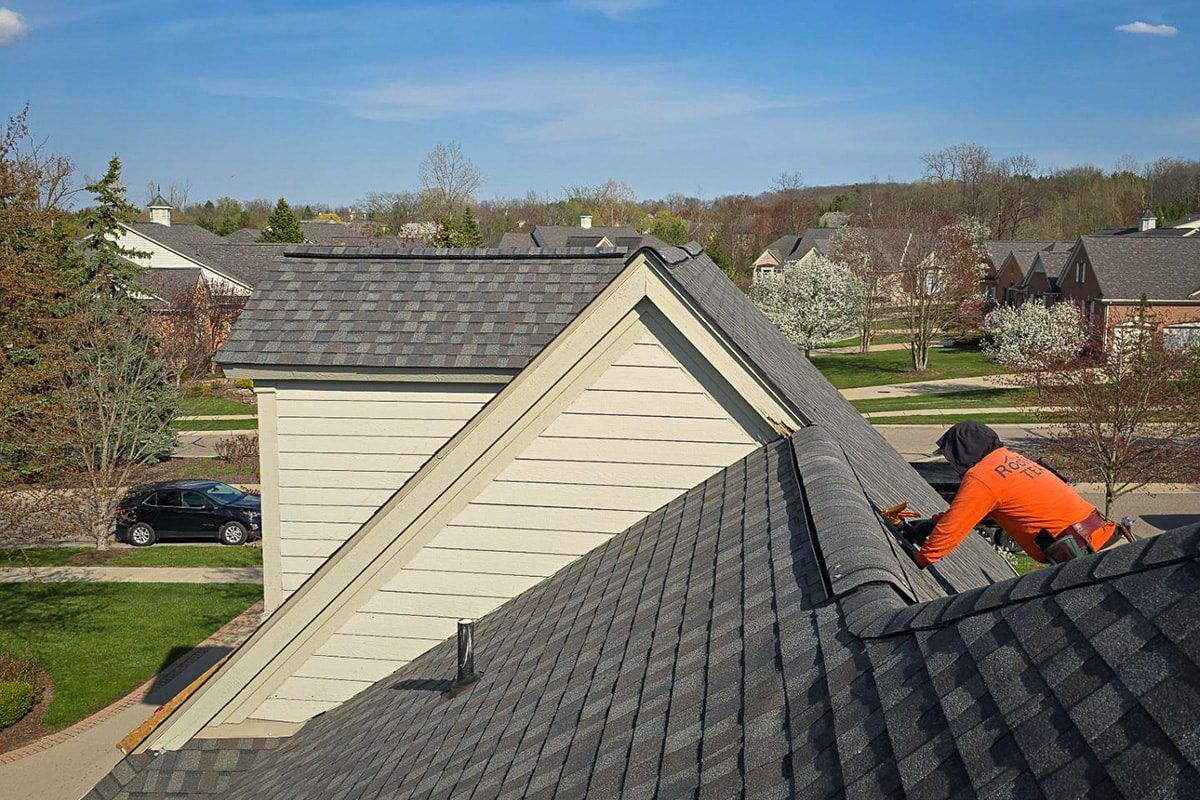Multi-family roof maintenance. Roofer repairing a gray asphalt shingle roof on a house in a suburban neighborhood.