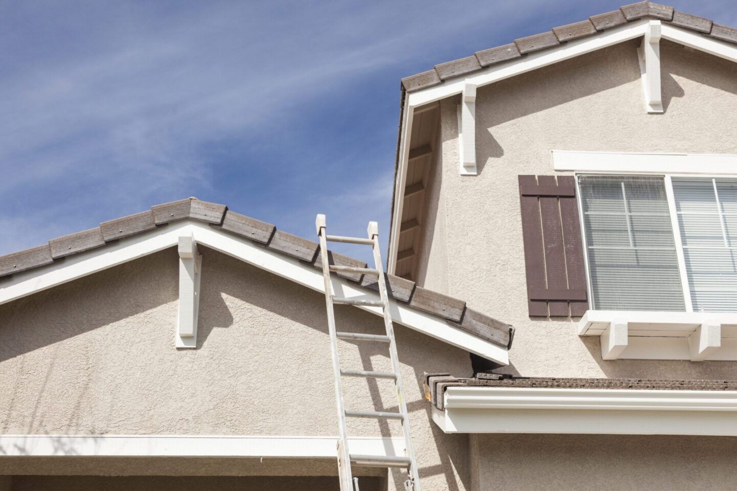 Ladder leaning against a freshly painted home with modern roofing details and clear blue sky.