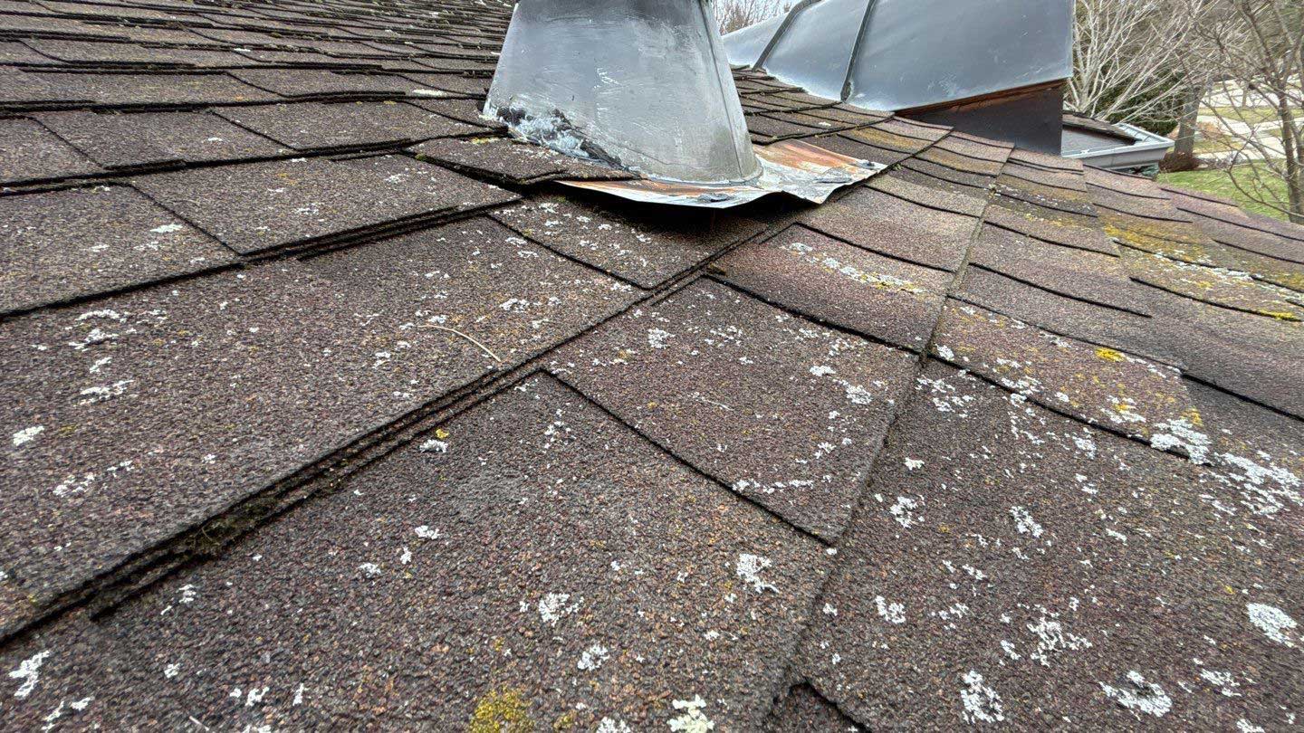 Close-up of an aged, damaged roof with missing shingles and a compromised chimney flashing.
