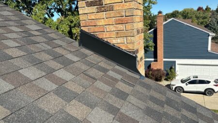 New black chimney flashing integrated into GAF architectural shingles during roof replacement project in Novi, Michigan.