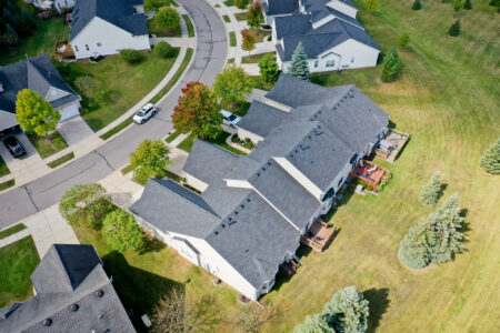 Aerial view of the Auburn Grove residential community featuring single-family homes with dark shingle roofs, private back decks, and landscaped green lawns.
