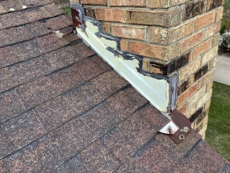 Deteriorated chimney flashing with exposed sealants and aging roofing materials on Novi home before replacement.