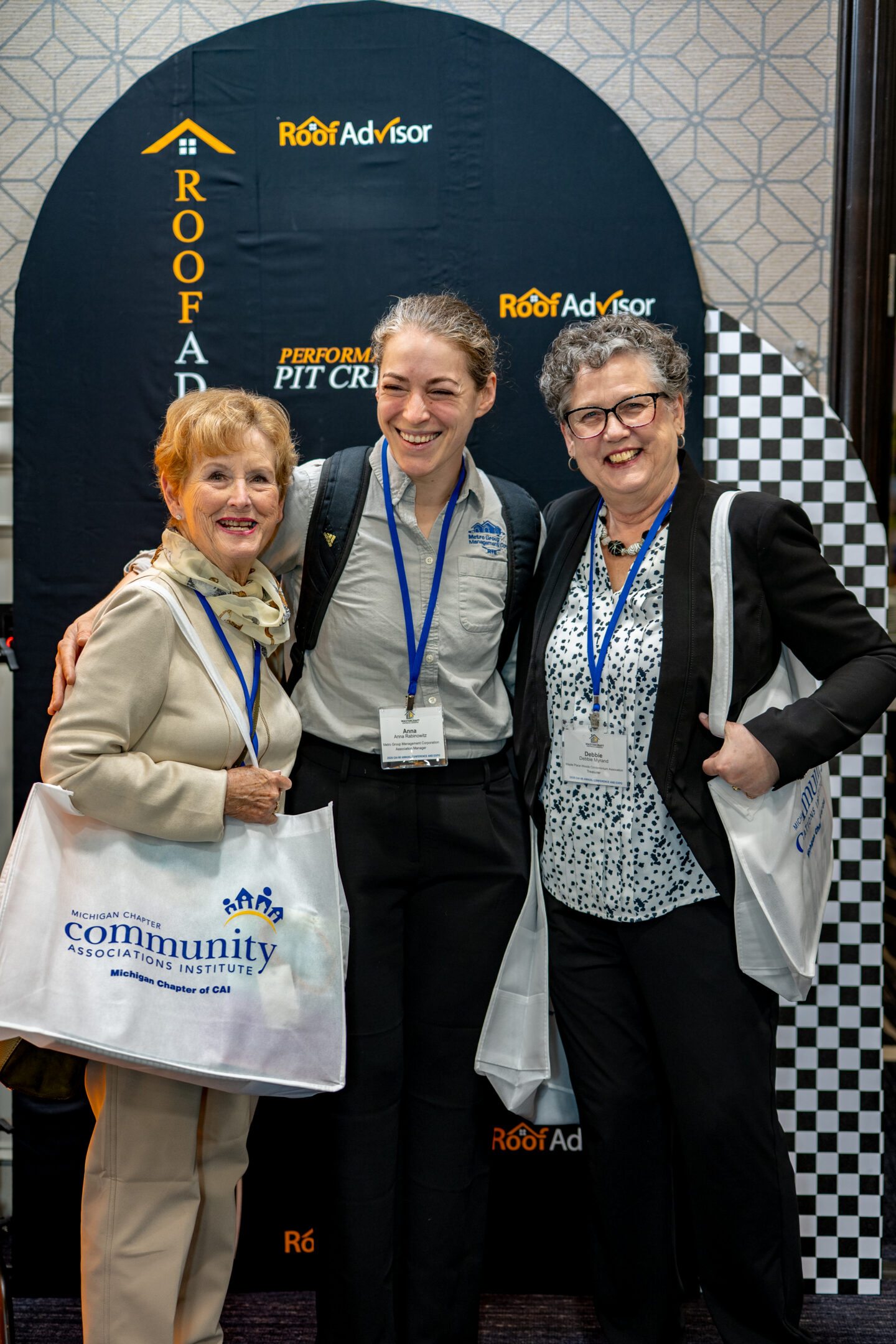 Three women pose in front of a Roof Advisor backdrop at a Community Associations Institute event. CAI2026012 captures a networking moment.