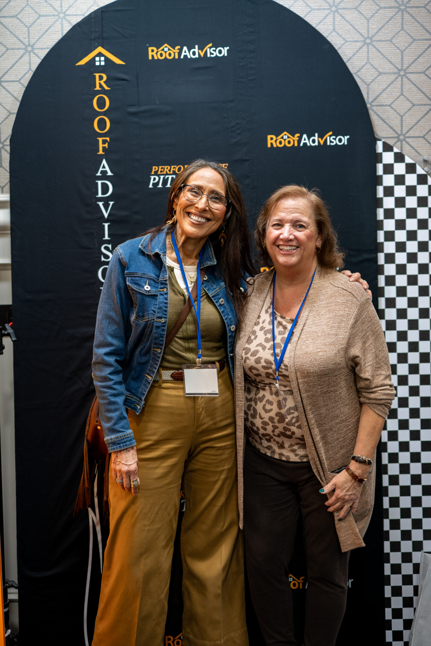 Two women smiling in front of a Roof Advisor banner at CAI2026017.jpg, showcasing roofing expertise and advisor connections.