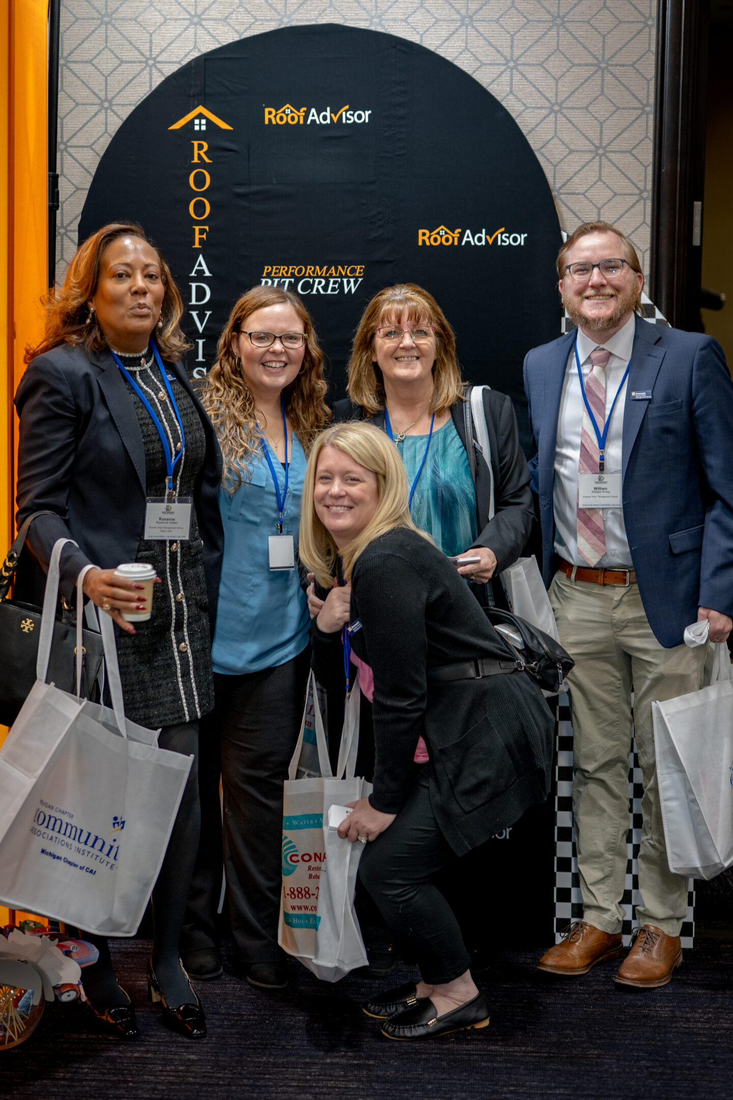 Group of five smiling people pose in front of a Roof Advisor backdrop. CAI202602 shows diverse professionals at an industry event, promoting roofing solutions.