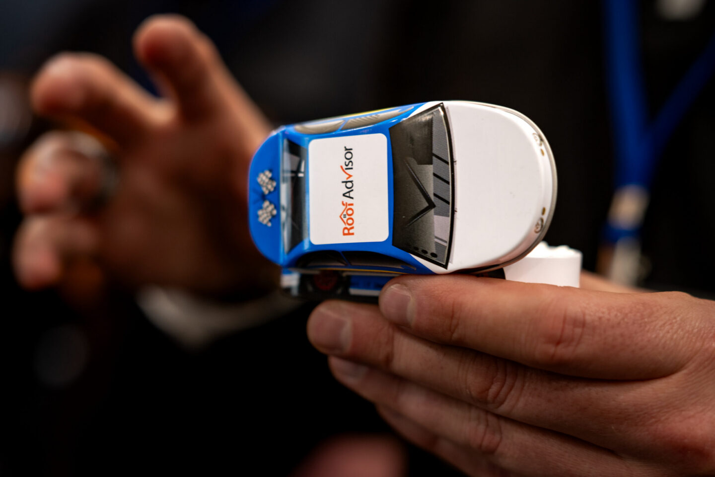 CAI2026023 image of a hand holding a Roof Advisor device shaped like a car, showcasing its design and branding. Roof Advisor is a roofing solution provider.