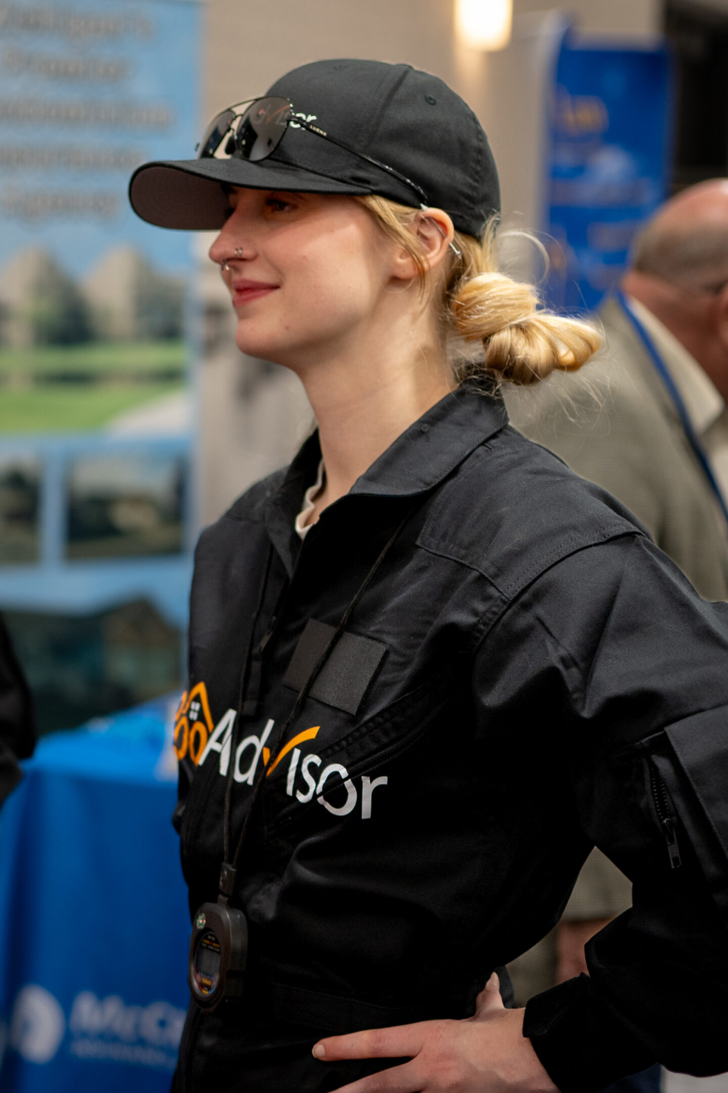 CAI2026027: Woman wearing a black uniform with the "Advisor" logo, baseball cap, and sunglasses on the brim. Blonde hair is tied back in a bun.