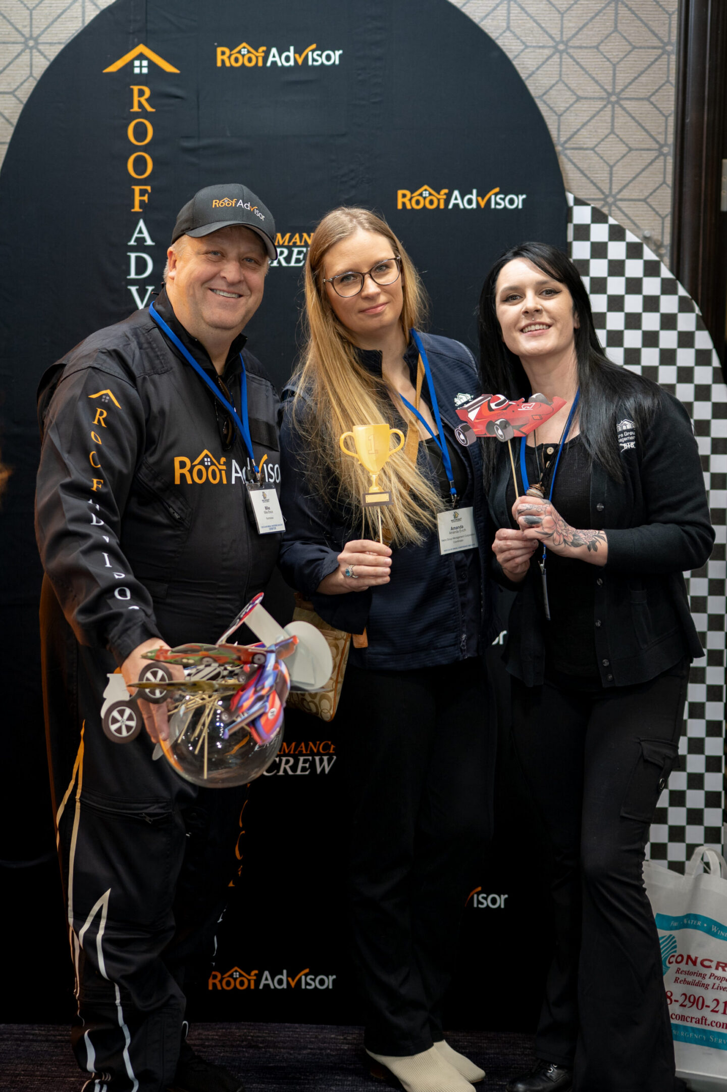Roof Advisor team members celebrate with trophies and a race car model. CAI2026031 showcases the team's success and camaraderie at an event.