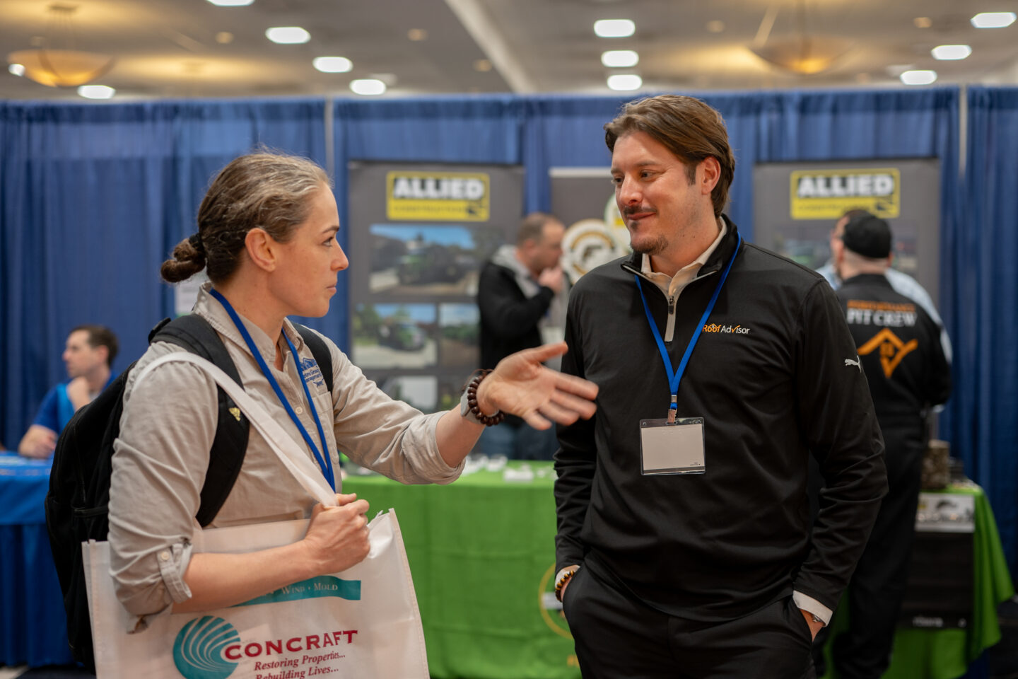 CAI202609: Two professionals conversing at a Concraft trade show booth, discussing property restoration and rebuilding after water, fire, or mold damage.