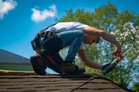 Roof Maintenance: Roofer using caulk gun on shingle roof. Professional home maintenance and repair services.