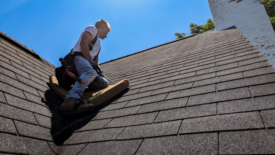 Roofer repairing roof damage. Man on roof fixing leak. Asphalt shingles.