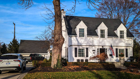 Plymouth MI home after roof replacement by Michigan Roofing Company. New dark grey roof on a white house. Professional roofing services for your home.