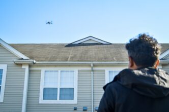 Drone roof inspection. Man watches drone inspect roof for damage. Roof health check.