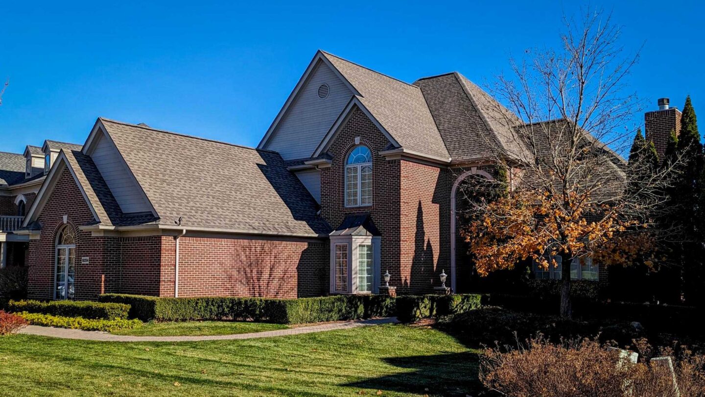 Residential shingle roof replacement on a brick house. Architectural shingle roofing on a luxury home with manicured lawn and landscaping.