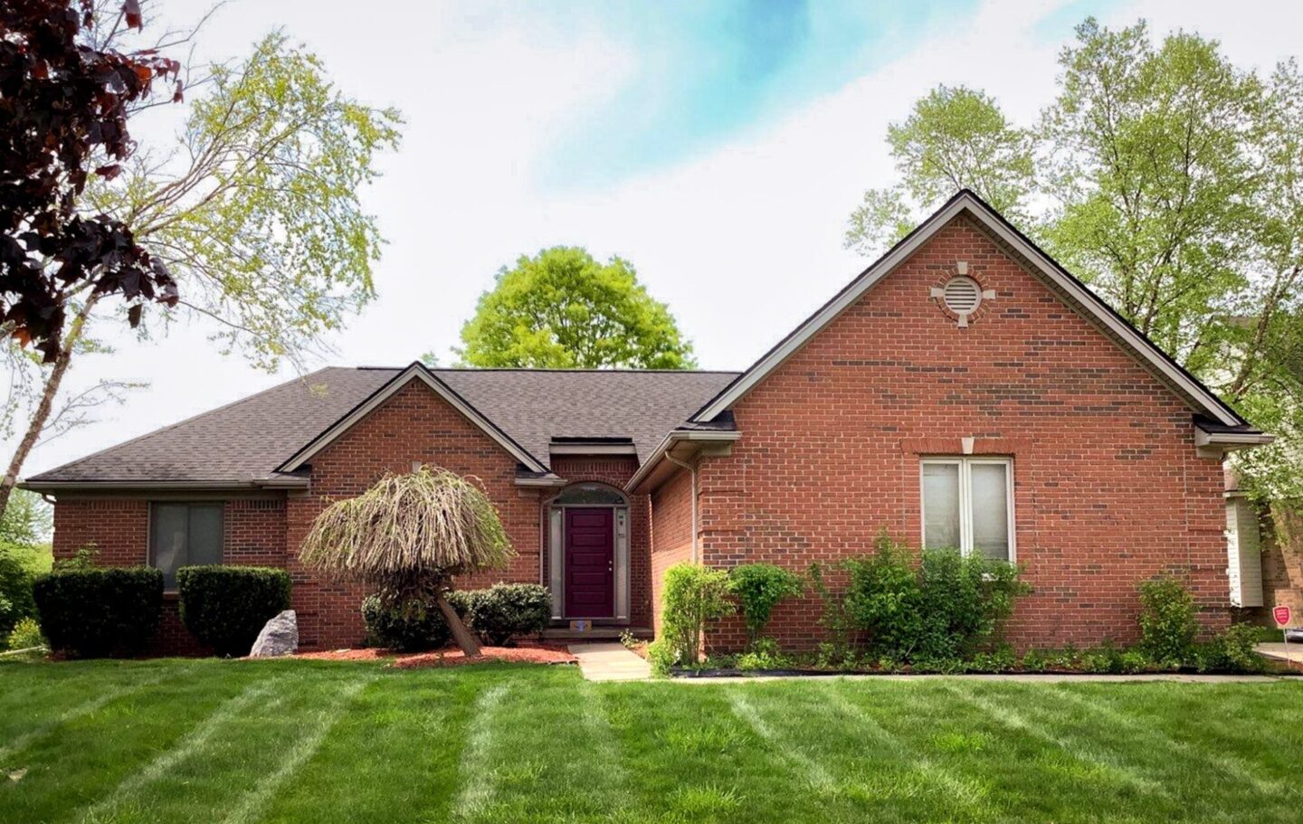 Taylor Mulberry Trail home featuring roof replacement. The brick home has a unique roof design and is surrounded by trees.