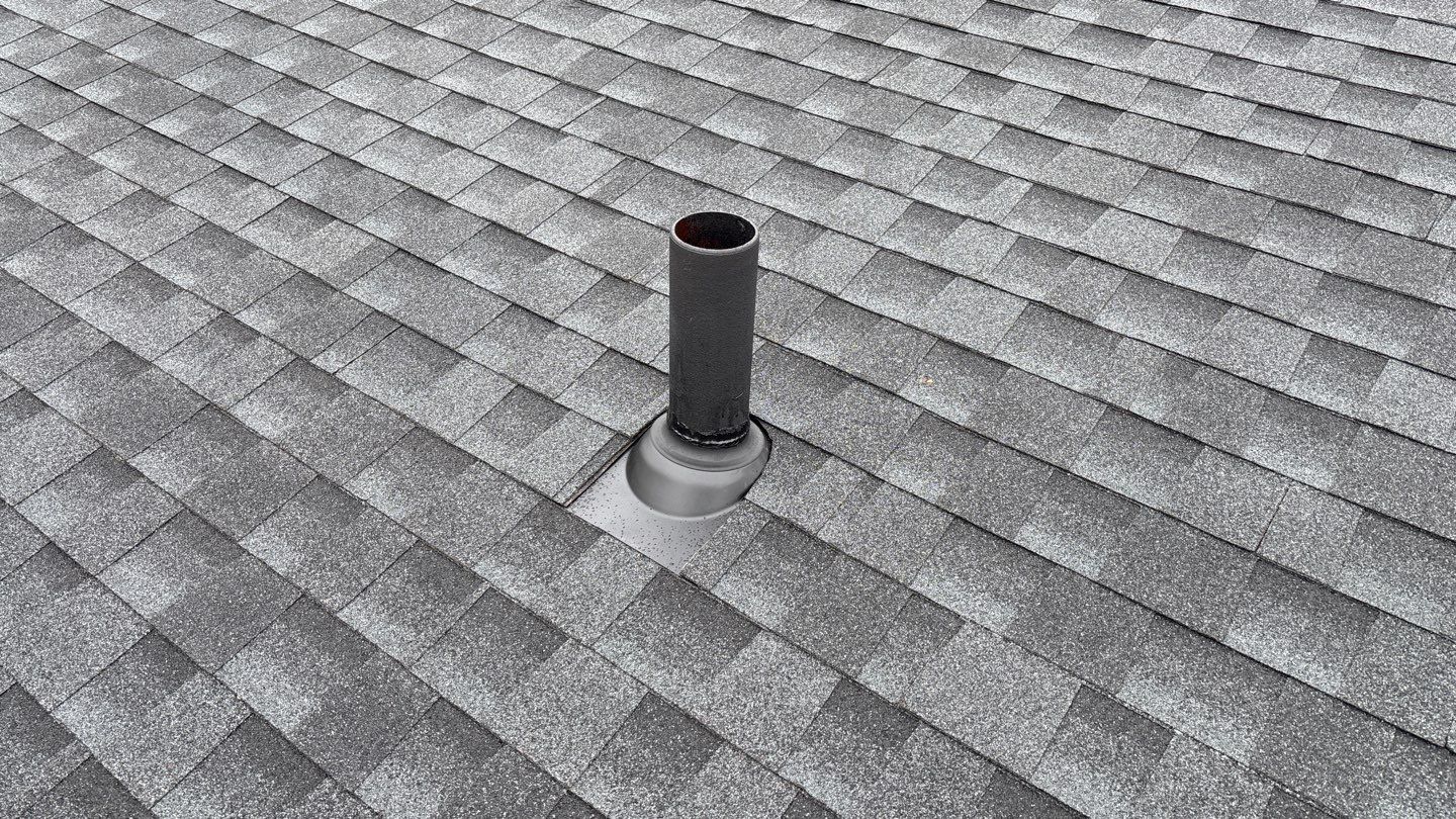 Close-up of a newly installed gray asphalt shingle roof in daylight with a single black vent pipe centered.