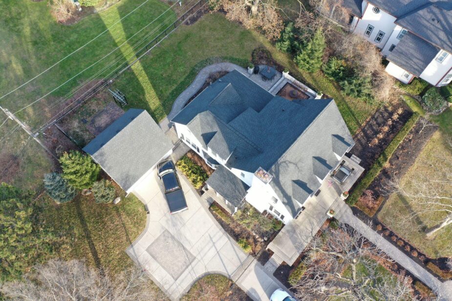 Aerial view of a Plymouth residential property featuring a newly installed dark charcoal shingle roof, a concrete driveway, and a black pickup truck parked