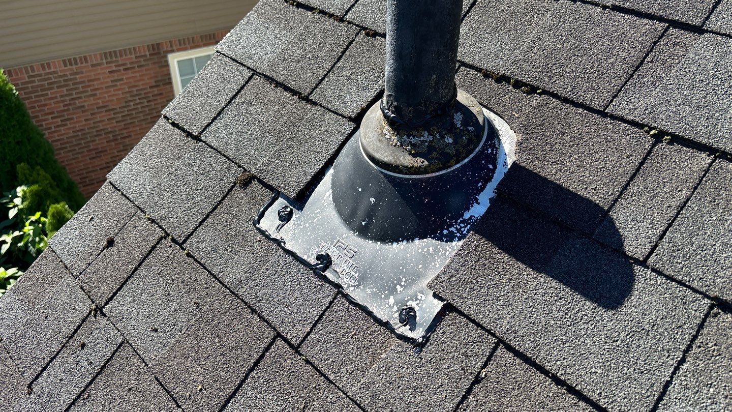 Roof vent pipe flashing on an asphalt shingle surface in Dearborn, featuring a labeled IPS Waterlite base with visible signs of weathering and oxidation.