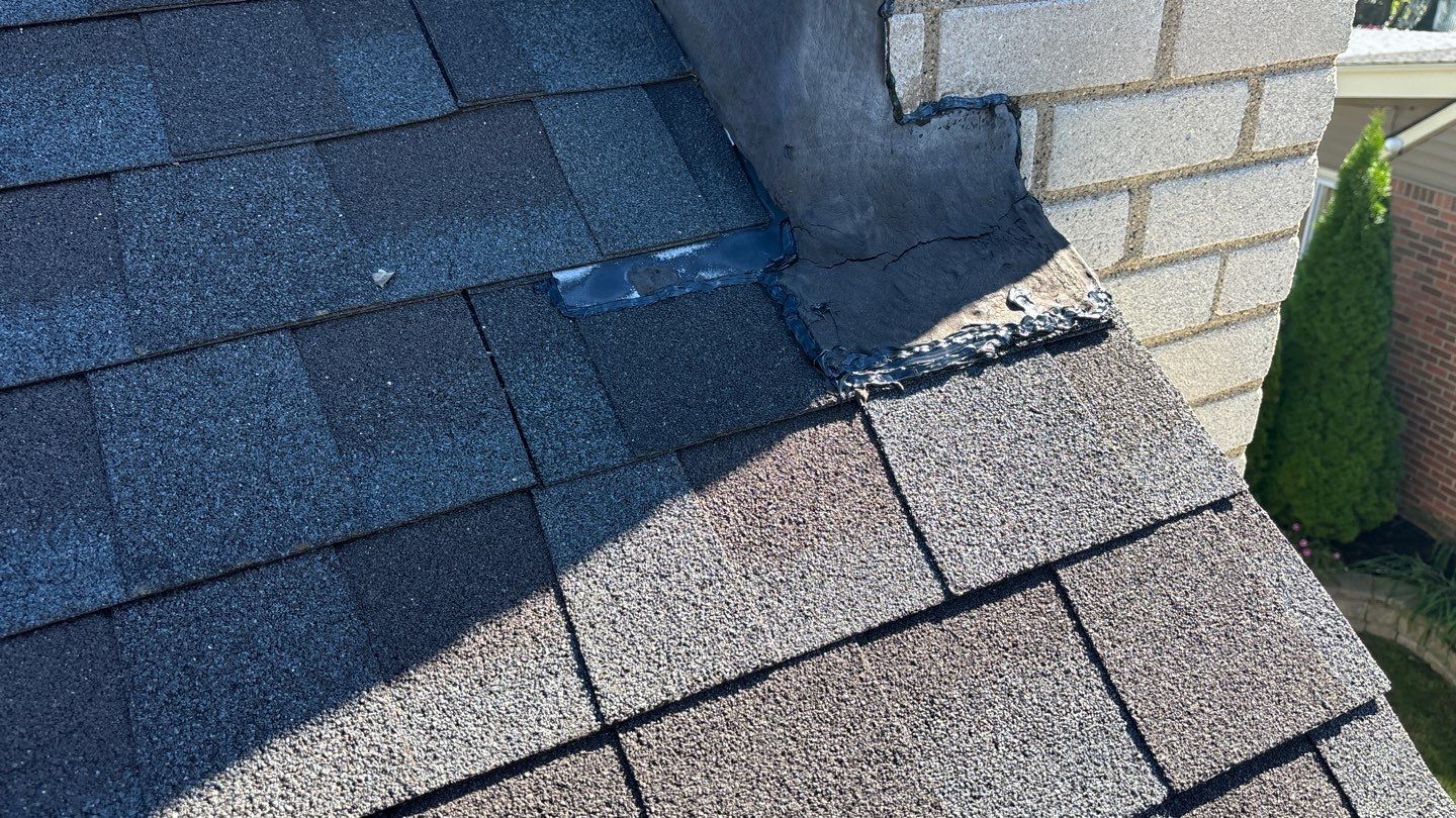 Completed roof repair in Dearborn showing new dark shingles installed against a brick chimney with smooth, clean flashing and professional sealant lines.