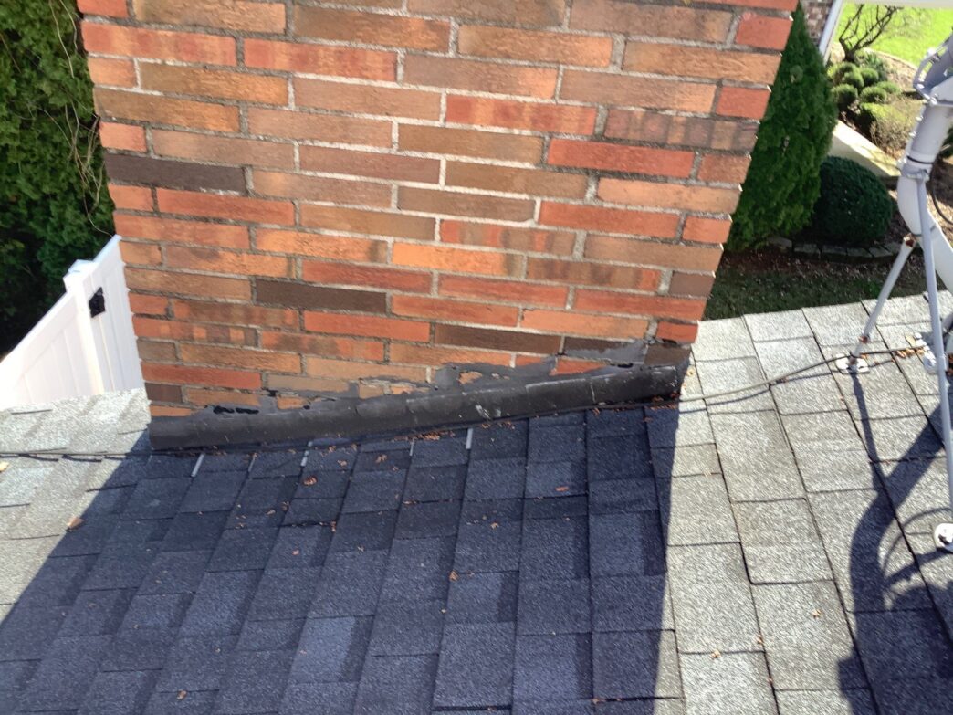Before roofing work on Andrea M's Clinton Twp home. Shows a brick chimney with damaged flashing and roof shingles needing 5-Star Roofing repair services.