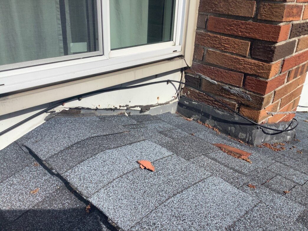 Roofing replacement. Deteriorated shingles near a window and chimney indicate need for roofing repair.
