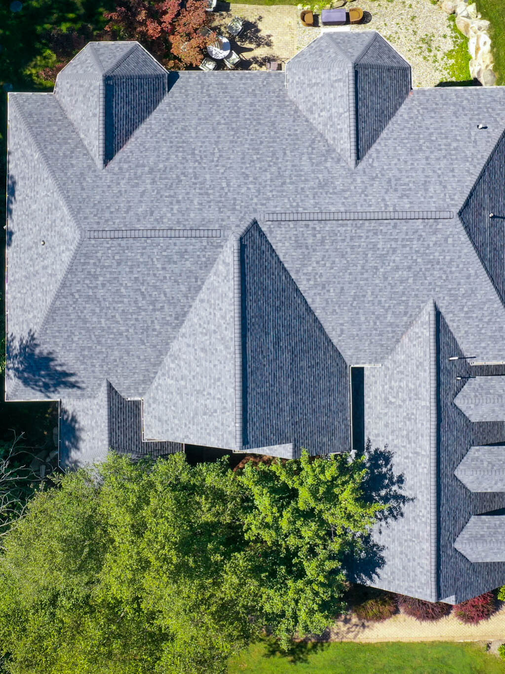 Aerial view of an Ann Arbor Pinecrest Estates home with a unique roof design, showcasing a roof replacement. Trees surround the property.