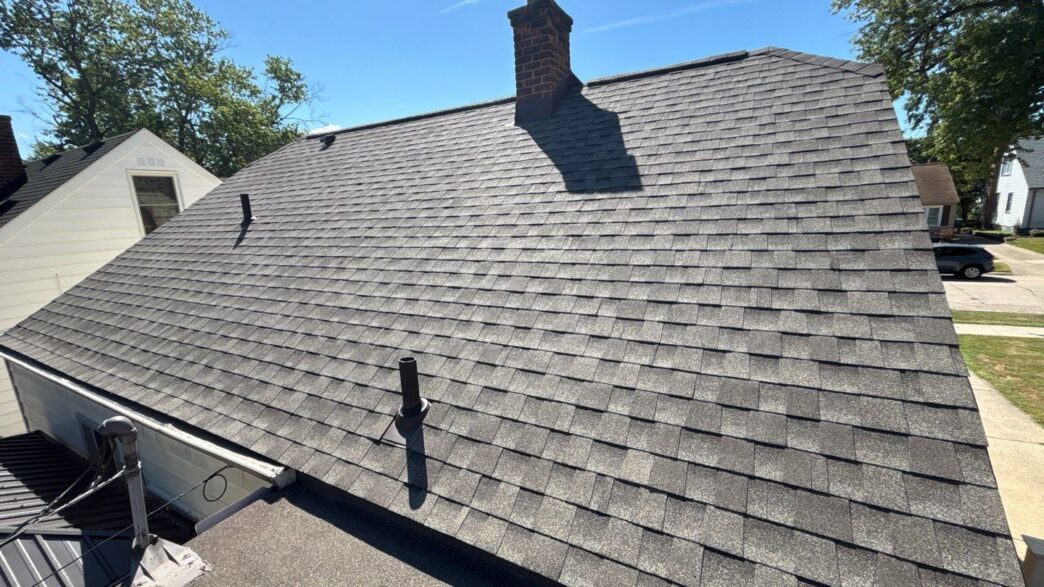 Roof with gray asphalt shingles and two vent pipes on a sunny day