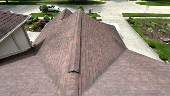 Brown shingle roof viewed from above, with intersecting roof sections and a residential street in the background
