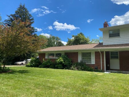 Ann Arbor roof replacement by Bill's, showcasing a newly installed roof on a brick home with green lawn, clear sky after the roof replacement project.