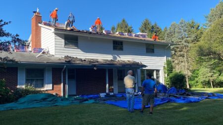 Ann Arbor roof replacement by Bill's Roofing shows workers on a roof removing old shingles and preparing for new roofing. Safety tarps are laid out below.