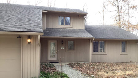 Before Canton roof replacement: Features a two-story beige house with a gray roof, visible front door, windows, and landscaping before renovation.