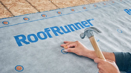 Integrity roof system roof runner on a house: Men installing MemBrain Continuous Air Barrier. Certainteed water resistant underlayment for shingles with a hammer. Roofing underlayment provides a critical water resistant layer.