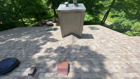 After Canton roof replacement by Bruce's, showcasing a chimney saddle, new shingles, and skylights. This improved roofing system offers lasting protection.