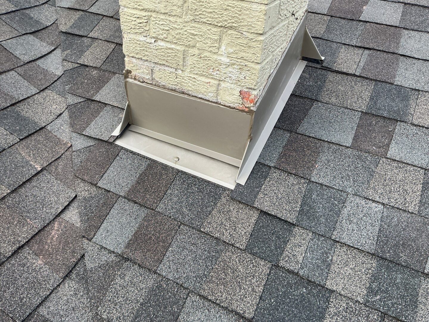 Chimney with metal flashing on a Sterling Heights roof featuring new asphalt shingles; part of a roof replacement and gutter installation project.