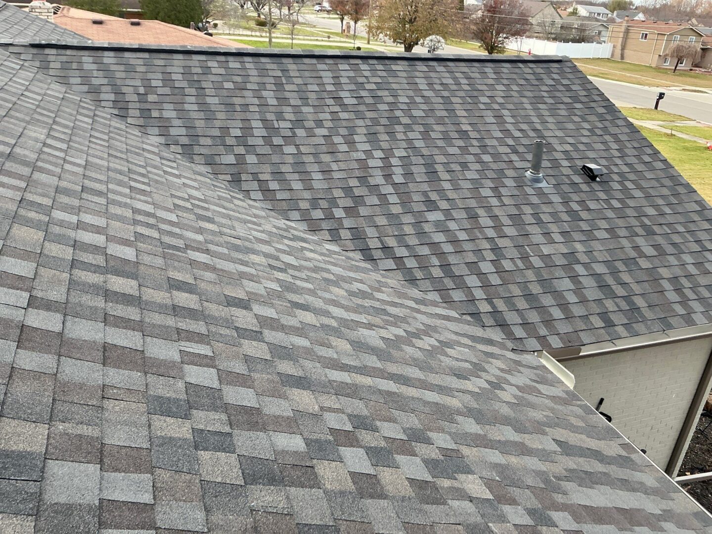 Overhead view of a Sterling Heights roof displaying gray and brown asphalt shingles after a roof replacement project, along with new gutters and a vent pipe.