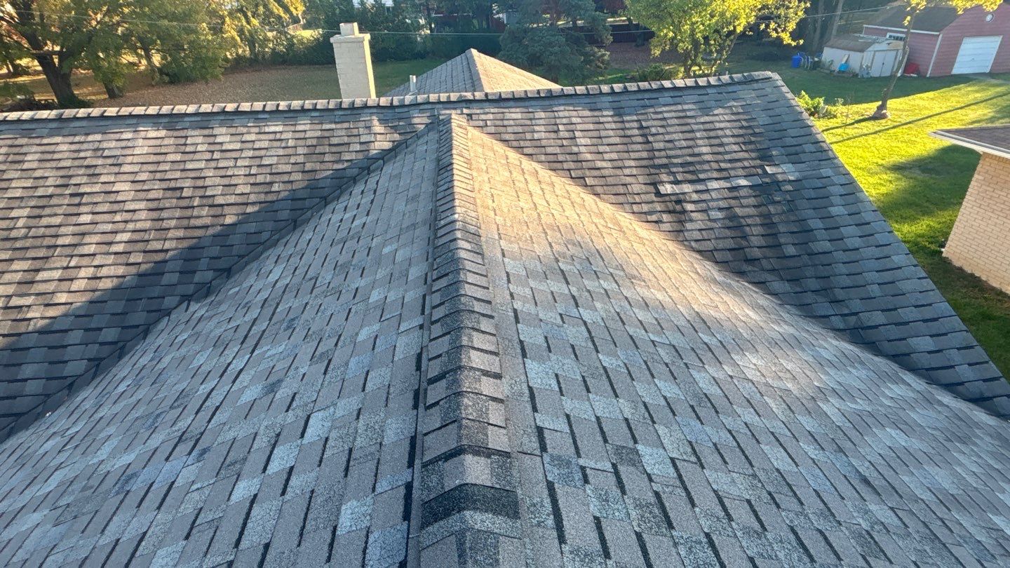 Wide view of an aging asphalt shingle roof with visible wear and damaged ridge areas