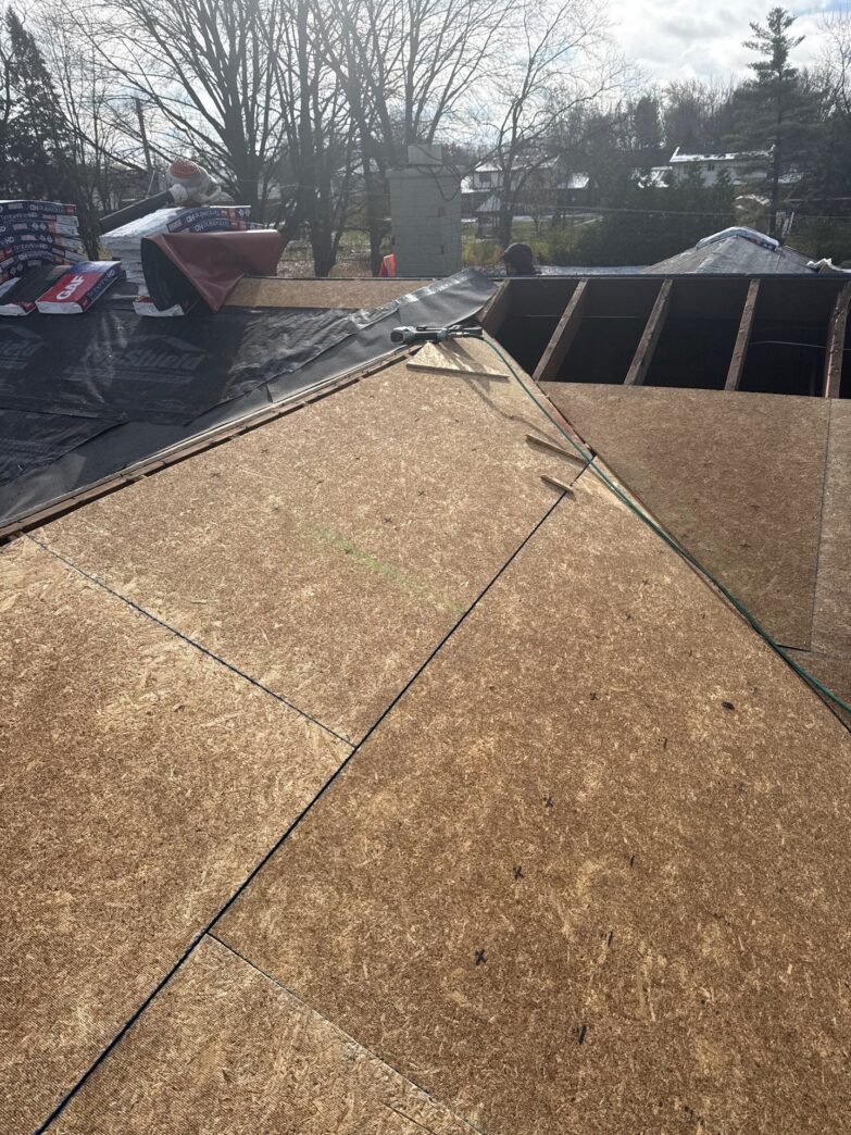 New OSB roof decking installation in progress with exposed rafters and partial underlayment application during residential reroof.