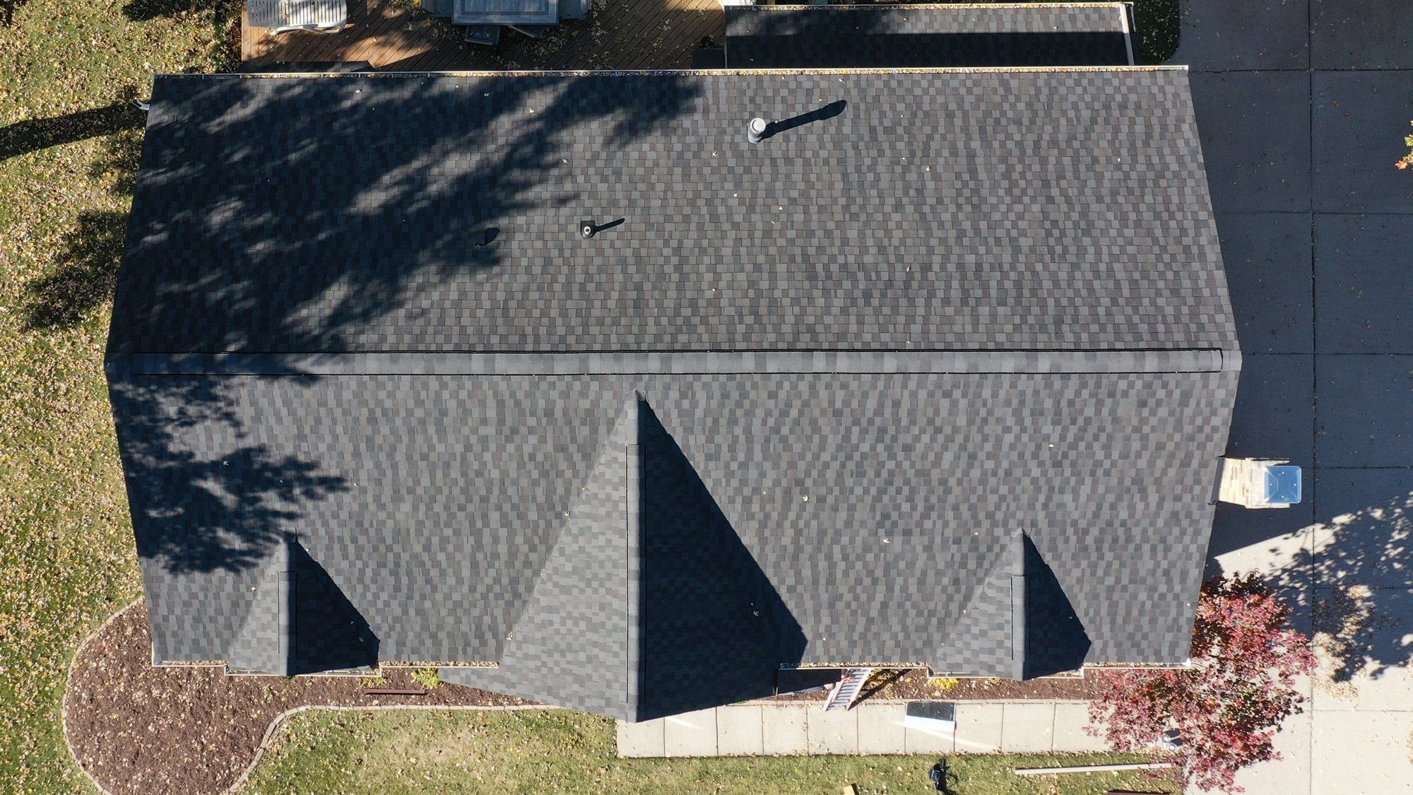 Aerial view of Evan B's Novi home after roof replacement by RoofAdvisor, showcasing new dark gray shingles & landscaping. Lawn and trees surround the house.