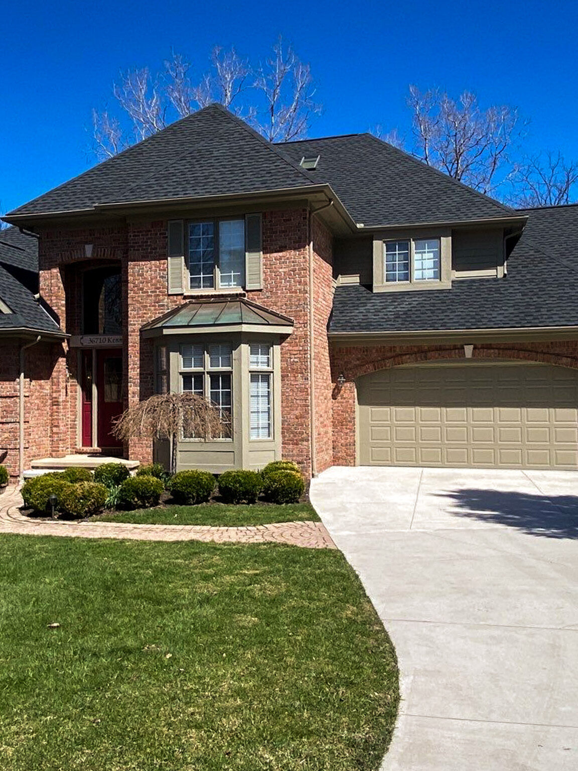 Farmington roof replacement. Brick home with a new roof installed in 2022. The home has a unique roof design and is surrounded by trees.