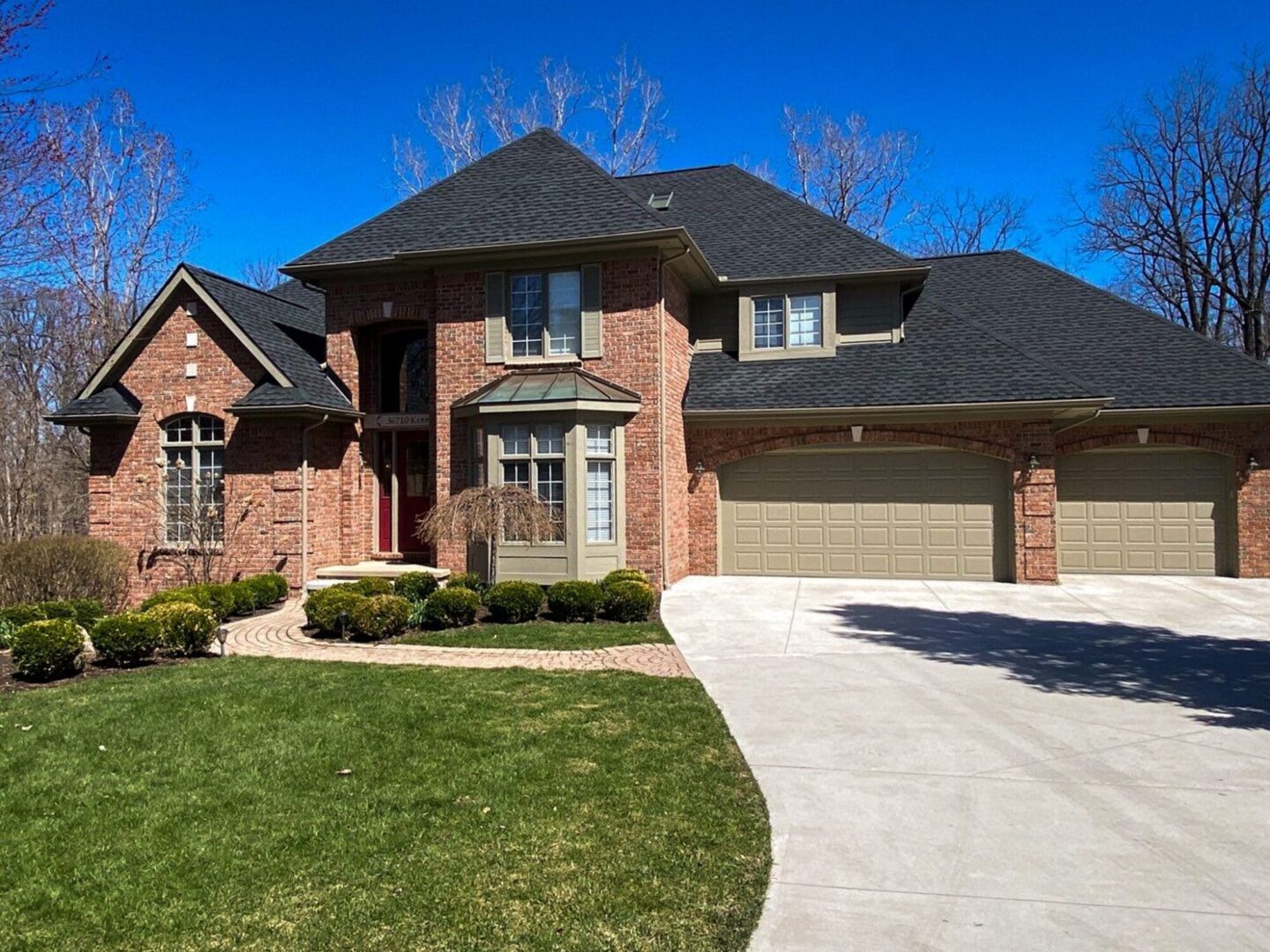 Farmington roof replacement. Brick home with a new roof installed in 2022. The home has a unique roof design and is surrounded by trees.