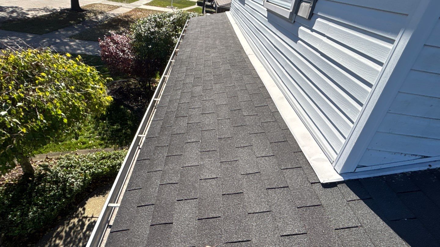 Dark asphalt shingles on a Brownstown roof are closely viewed from above, showing the texture and pattern of the roofing material near the house siding.