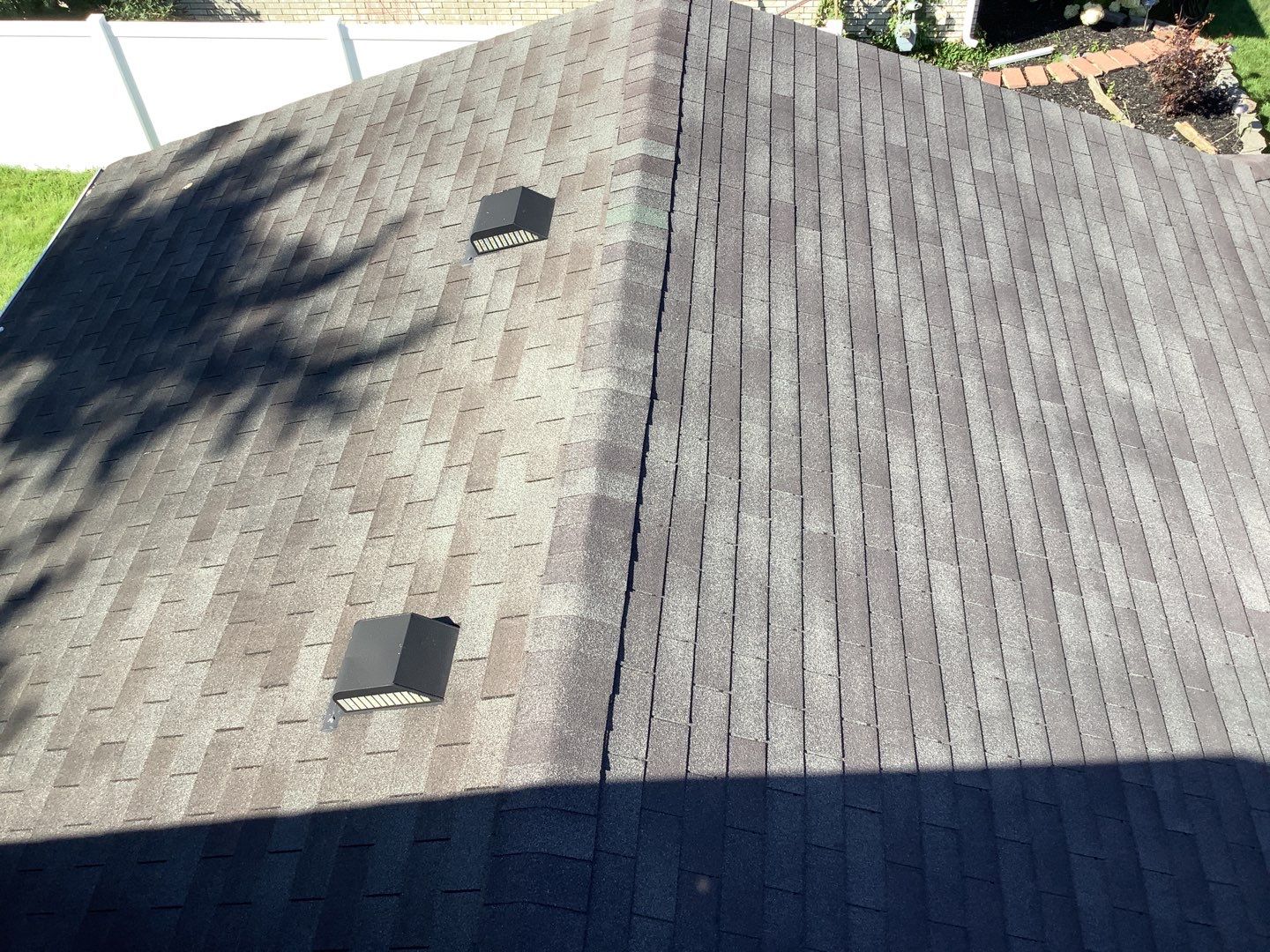 Before Brownstown roof replacement: Aerial view of an asphalt shingle roof needing replacement, vents are visible. Tree shadows cover part of the roof.