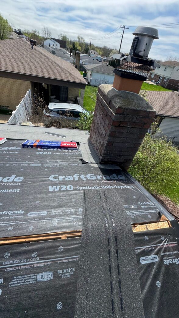CraftGrade underlayment on roof deck near a chimney. Blue shingle package lying nearby. Shows roof repair process.