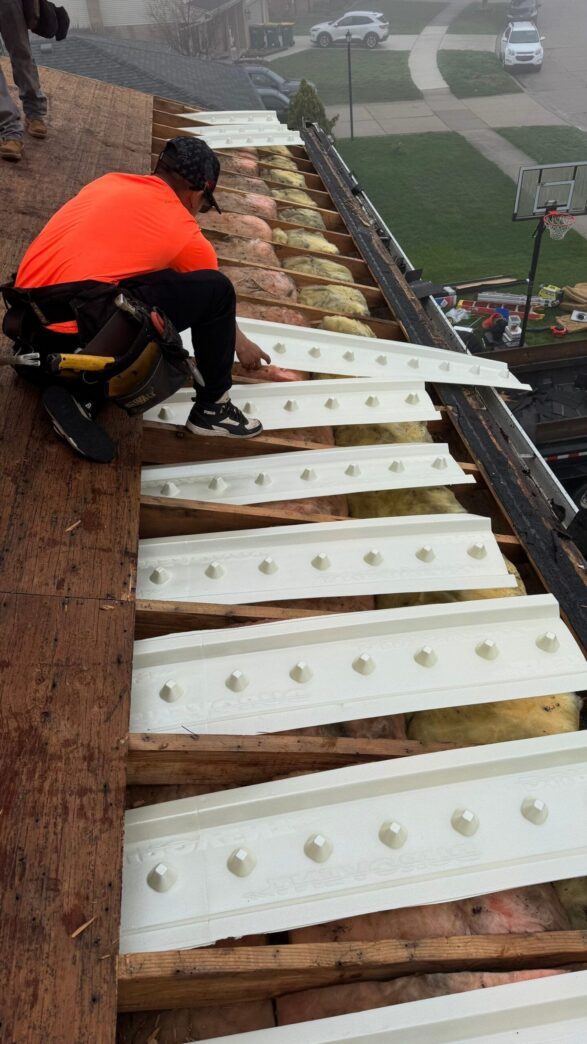 Roof repair in Brownstown after wind damage: Roofer installing white drip edge flashing on exposed roof rafters with insulation visible. Residential neighborhood.