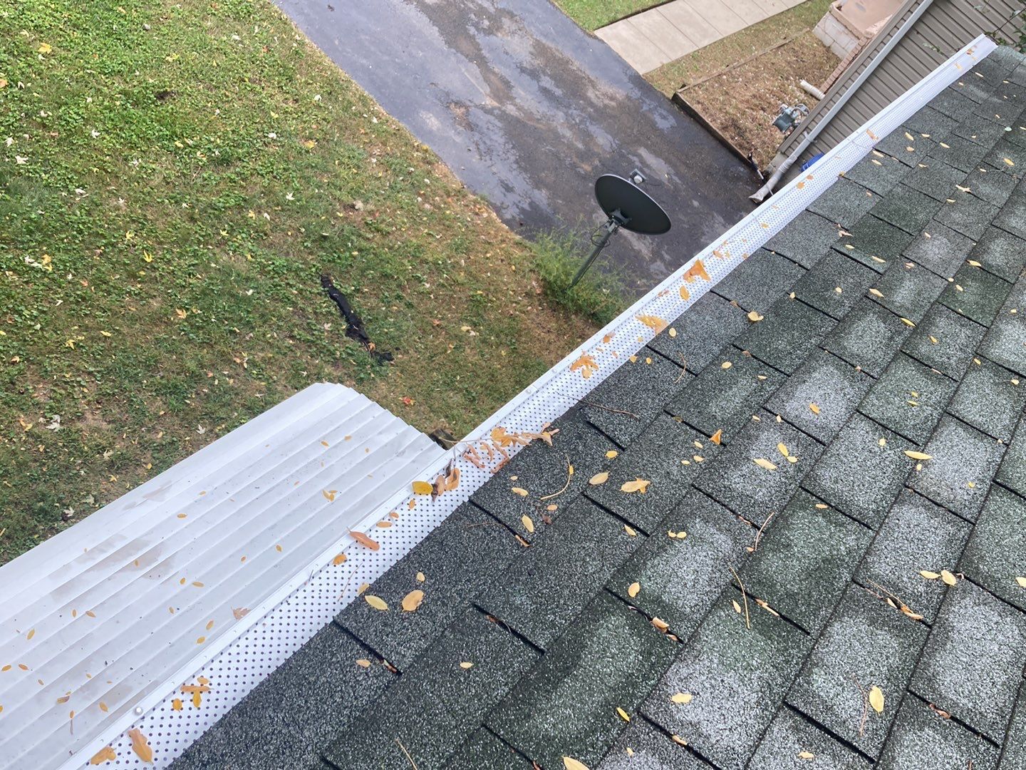 After Redford roof project showing gray shingles with leaf guard installation; autumn leaves are on the roof and along the gutter system, protecting it from debris.