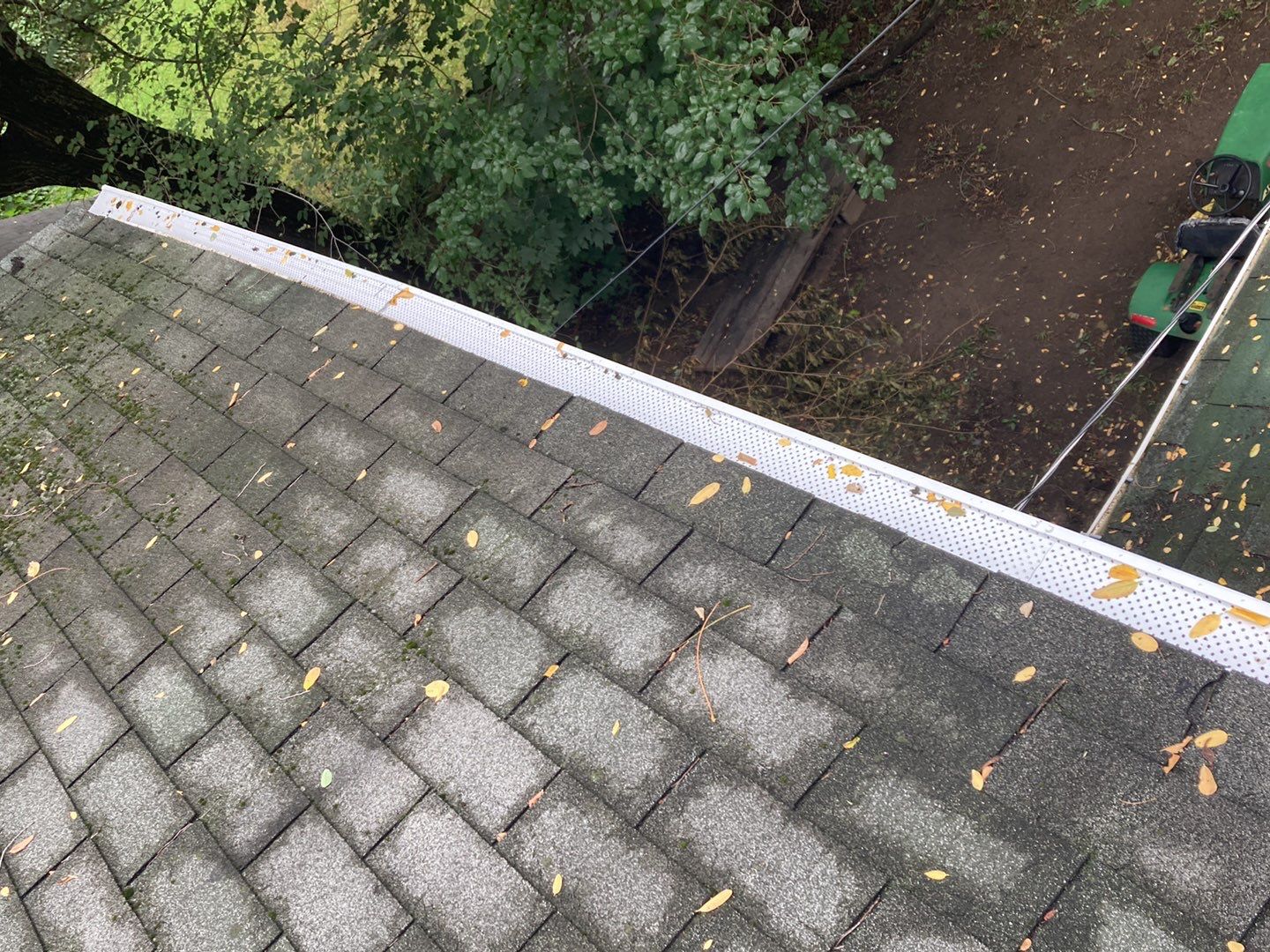 Redford roof and gutter with leaf guards showing fall leaves on the roof and in the gutter system. The roof is gray and the gutter is white with small holes.