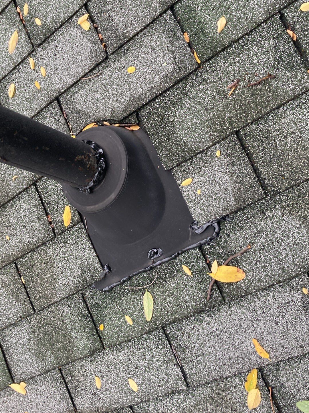 Gray Redford roof shingles surround a black pipe flashing; fall leaves are lightly scattered on the roof. Roof repair work is visible.