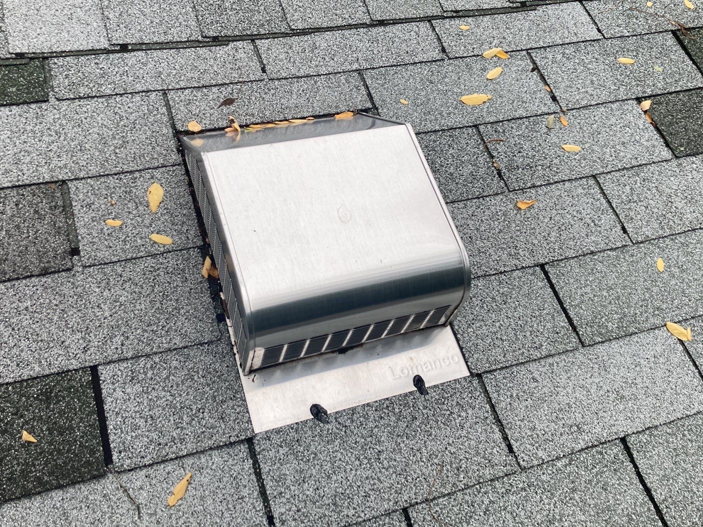 Close-up of a Redford roof with a Lomanco vent installed; gray shingles are visible around the vent with autumn leaves scattered about. Roof repair completed.