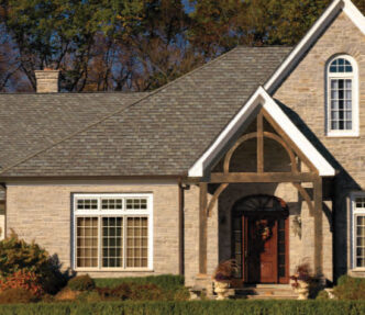 Featured project example: GAF Roofing Camelot II designer shingles in Weathered Timber color. Example of an asphalt shingle roof on a stone house with a timber framed porch.